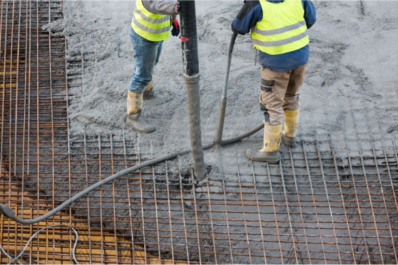 Concreters pouring concrete over steel reinforcing mesh